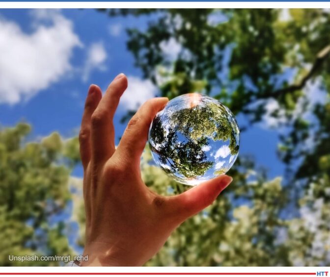 Clear blue sky, green tree leaves, a hand holding a crystal orb reminiscent of the earth